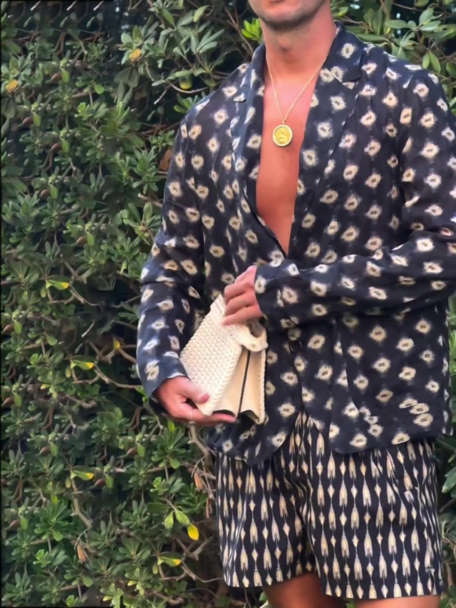 Man in the printed shirt-jacket and shorts in front of a green hedge