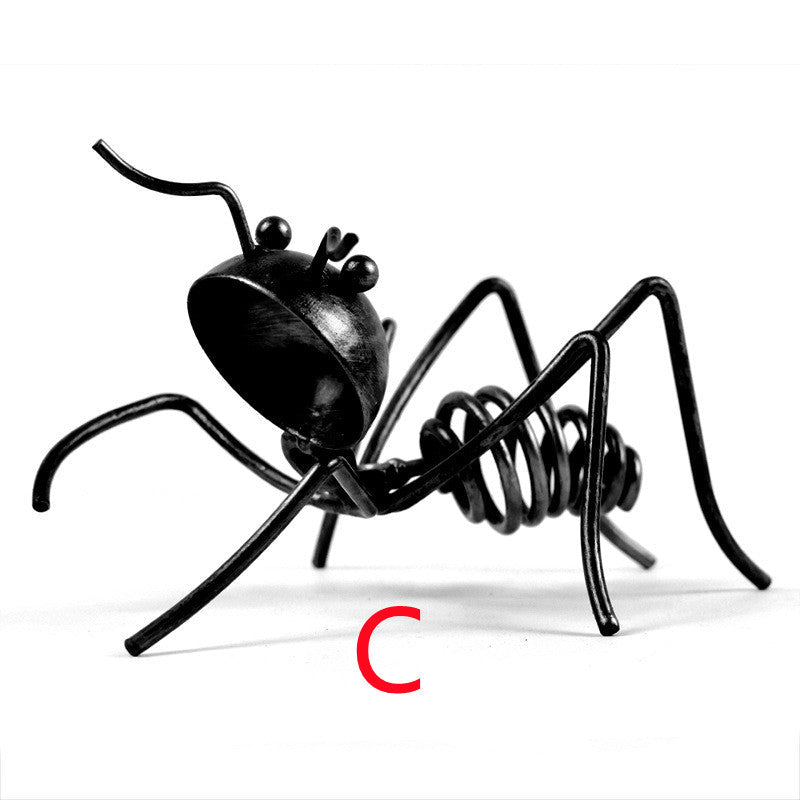 Black metal ant in pose C, crouching with its head tilted, marked with a red letter C