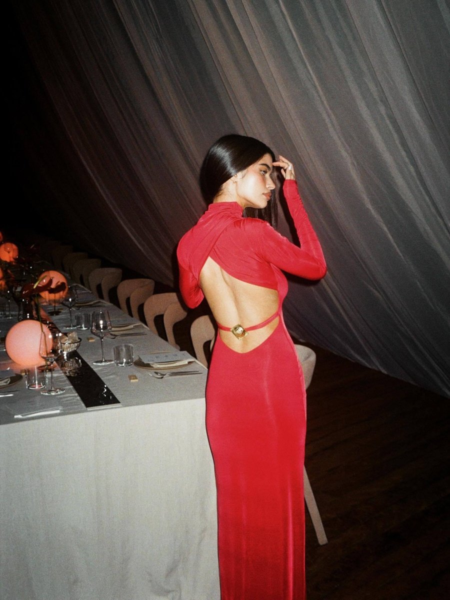 Red version of the open-back maxi dress next to a set dinner table