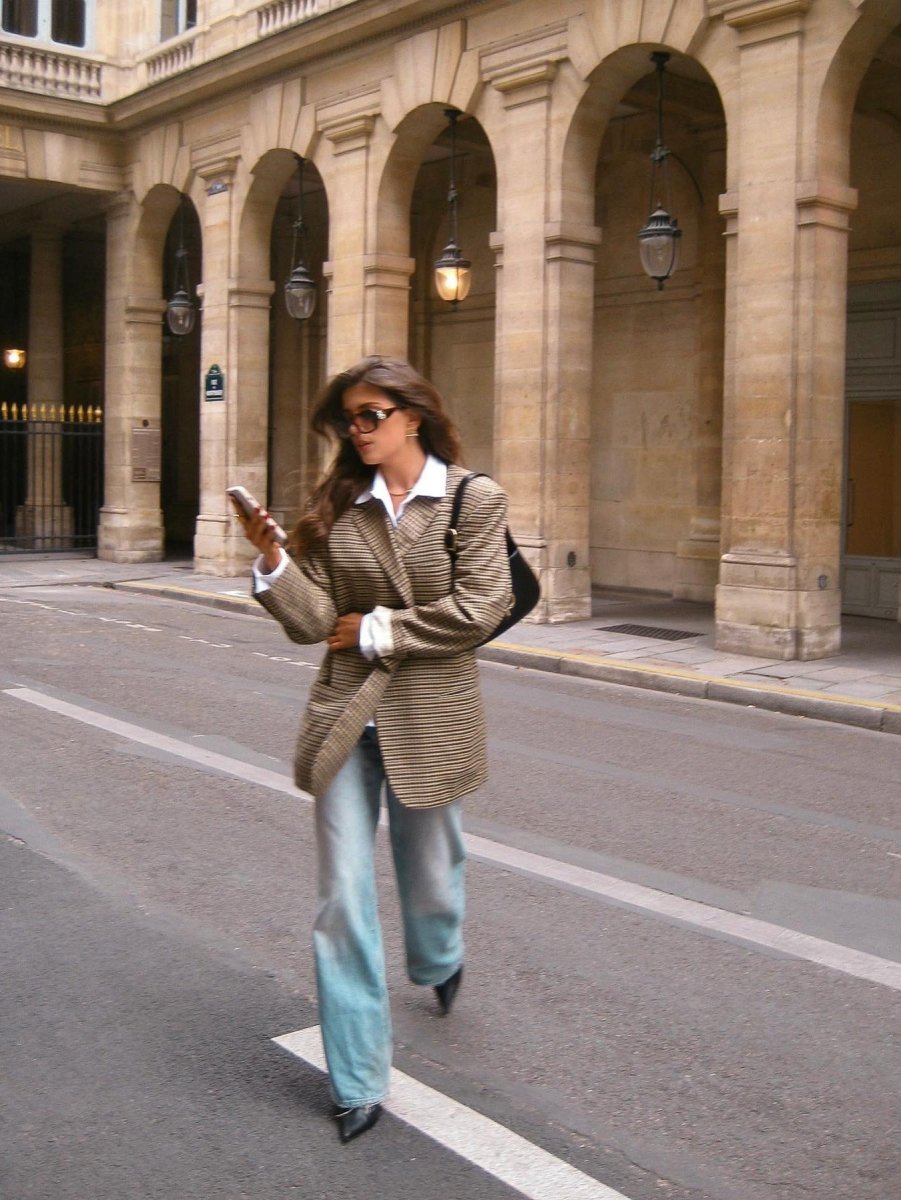 Model in the brown check blazer and jeans crossing a street, arcades behind her