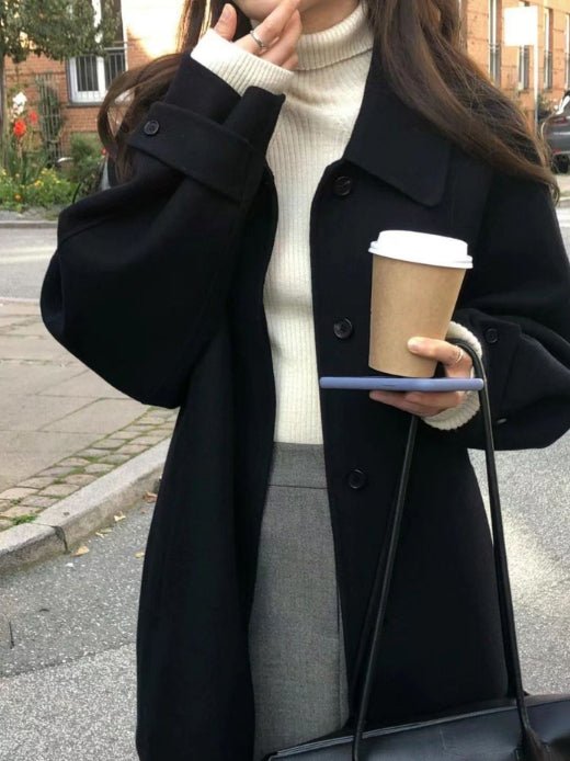 Navy oversized coat over a cream roll neck and grey skirt, coffee cup in hand