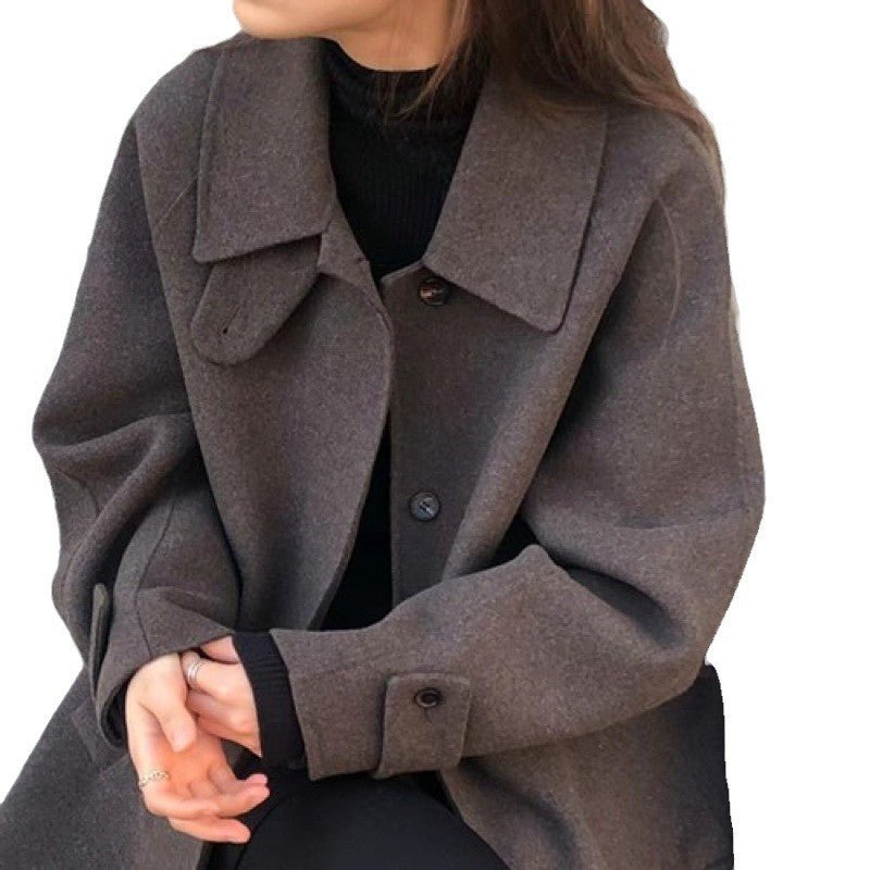The dark brown coat cut out on a white background, hands folded at the waist