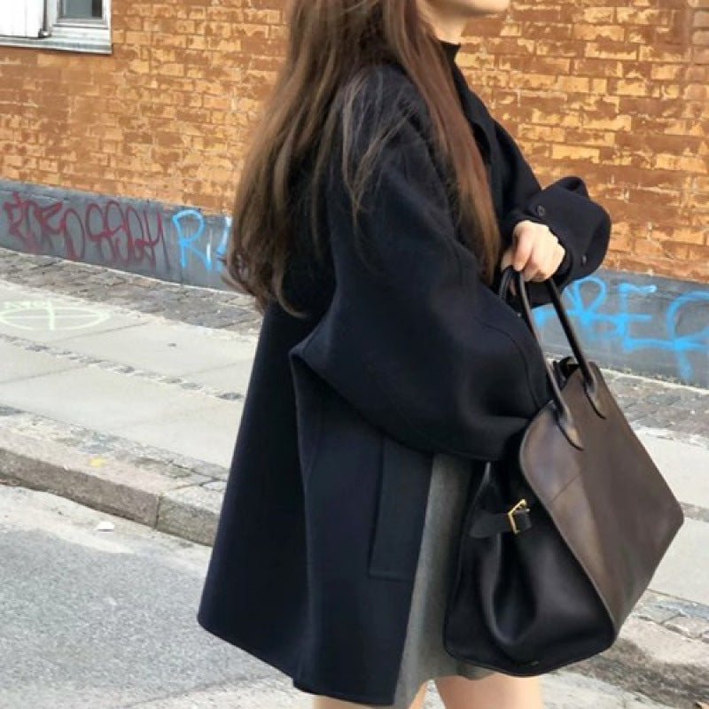 Side view of the navy coat with dropped shoulders, a large dark bag on the arm