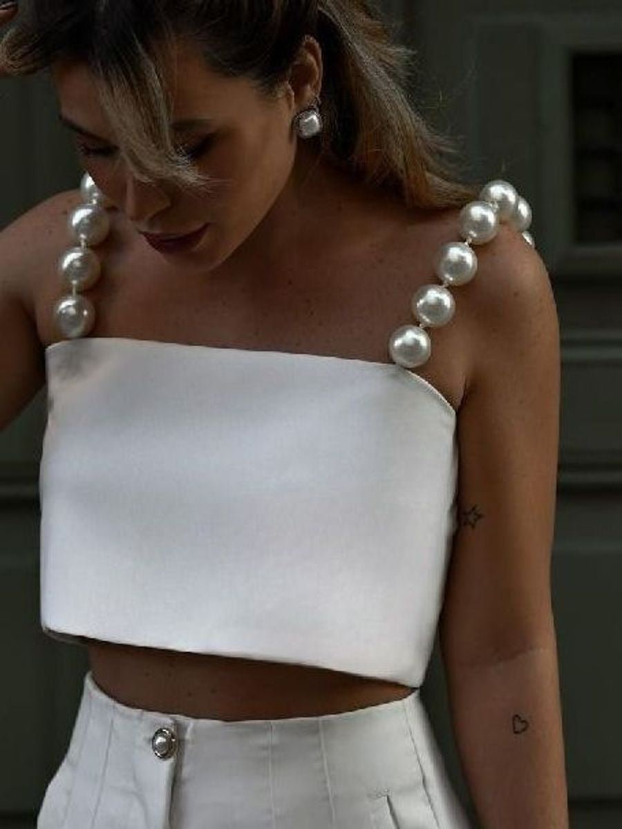 Woman in the white bandeau crop top with straps of large pearl-look beads, white trousers