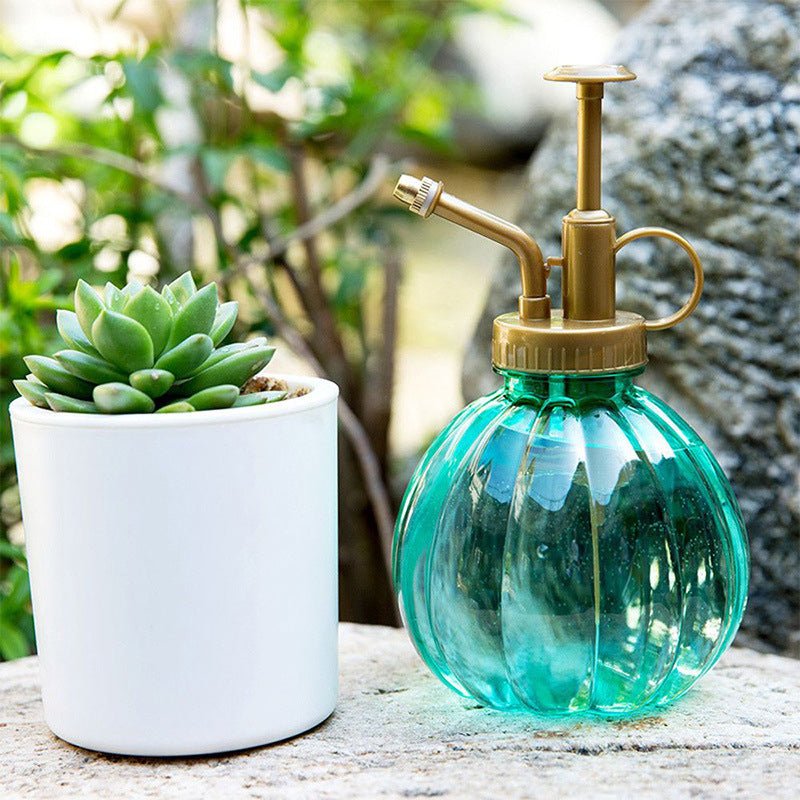 Groene plantenspuit naast een kleine vetplant in een witte pot