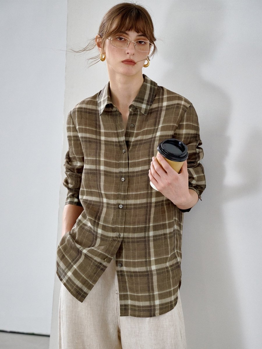 Model in the check shirt with sleeves pushed up, holding a coffee cup, leaning against a white wall