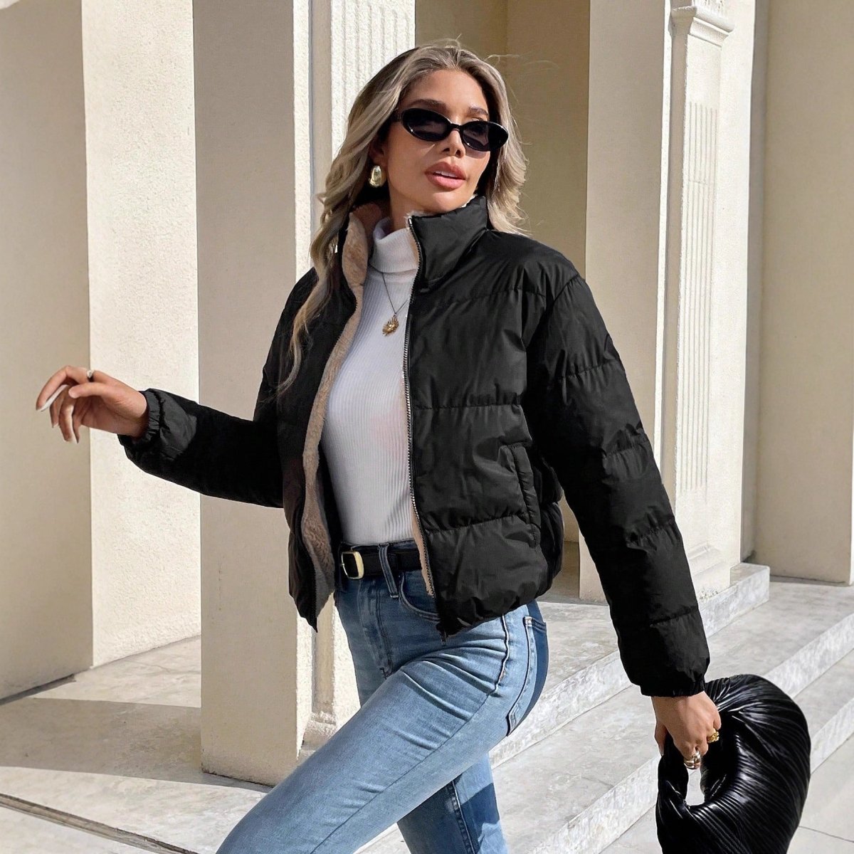 Woman in a cropped black puffer jacket worn open over a white roll-neck and light jeans, the cream inside visible at the zip