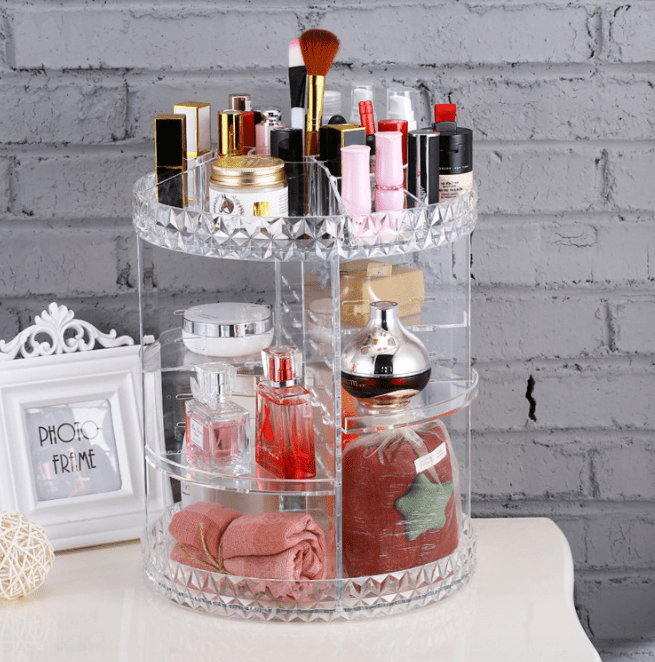 Clear rotating makeup organiser with a diamond-pattern rim, filled with lipsticks, brushes and bottles on a white dresser