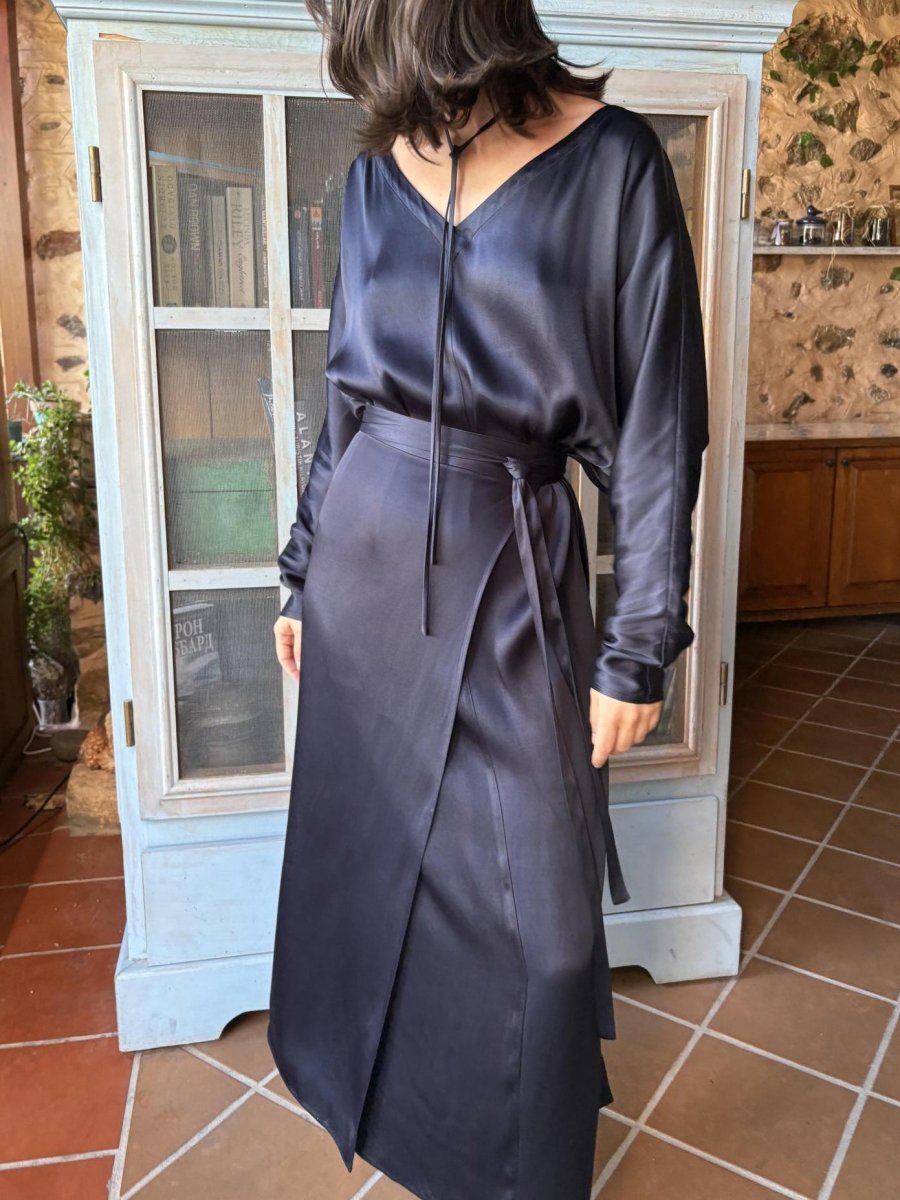 Woman in a long navy blue satin-look dress with V-neck and tie belt, standing in a tiled kitchen