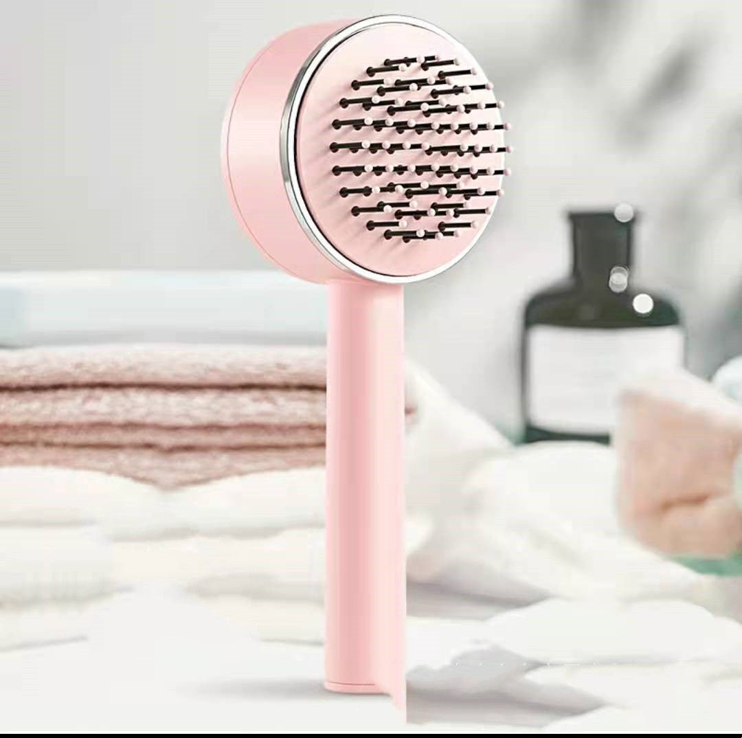 Pink self-cleaning hairbrush standing upright in front of folded towels