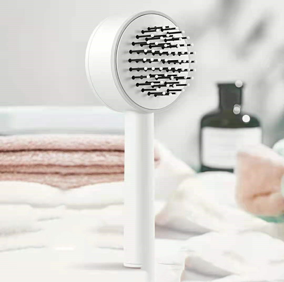 White self-cleaning hairbrush standing upright in a bathroom, round head with dark ball-tipped pins