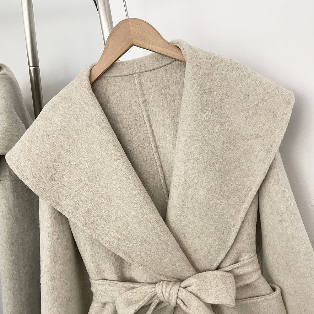 Close-up of beige short wrap coat with wide collar and tie belt, front view on hanger