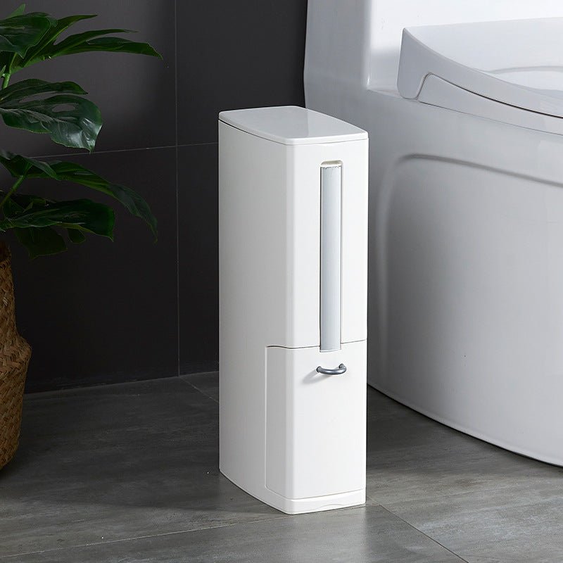White slim bathroom bin between a toilet and a plant on a grey tiled floor