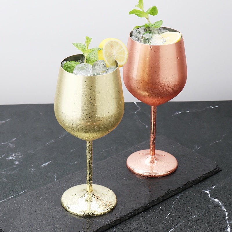 Stainless steel wine glasses in gold and rose gold, filled with ice, lemon, and mint, placed on black slate tray