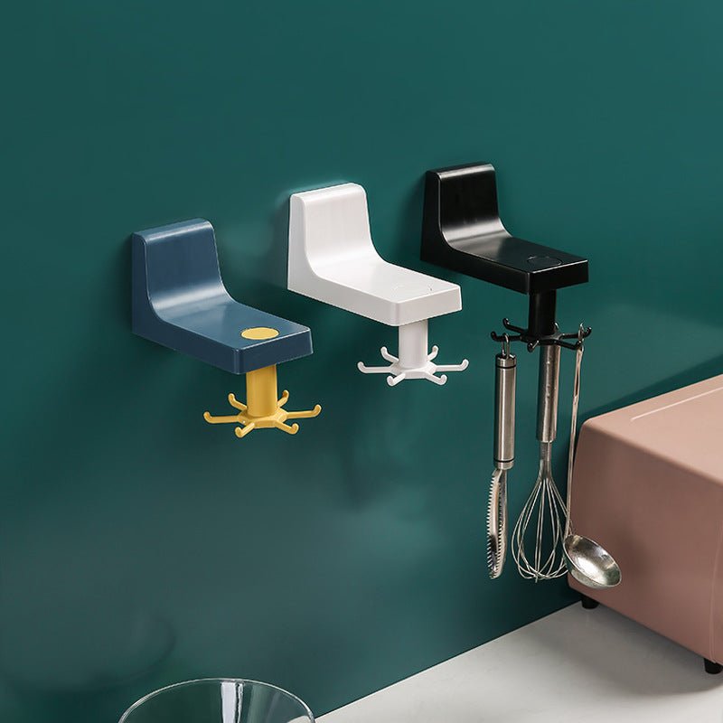 Three kitchen wall hook brackets in blue, white and black on a dark green kitchen wall, a whisk and ladles hanging from the black one