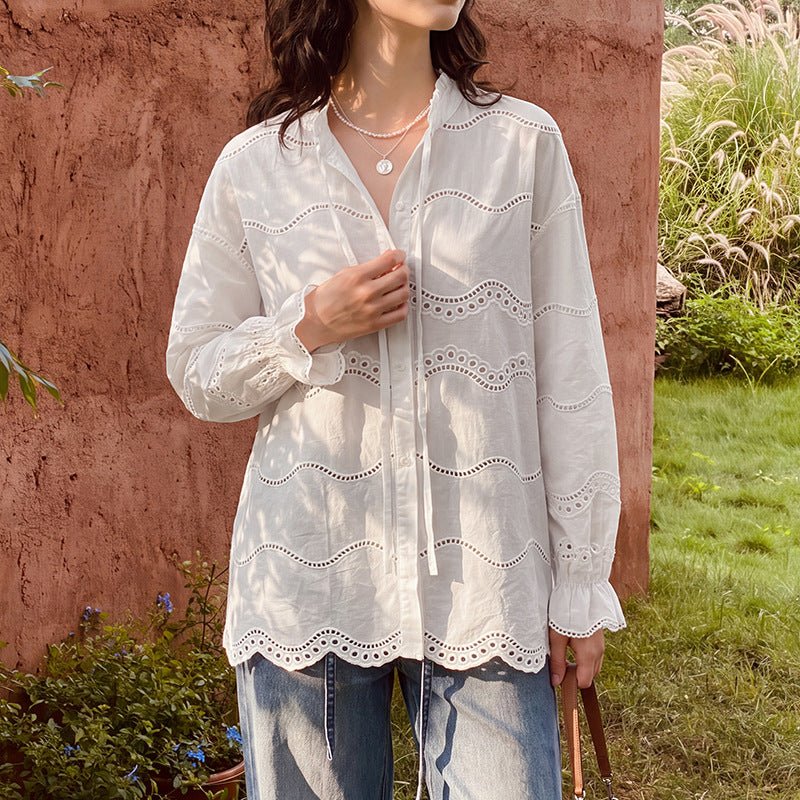 Off-white eyelet blouse worn loose over wide jeans against a terracotta wall
