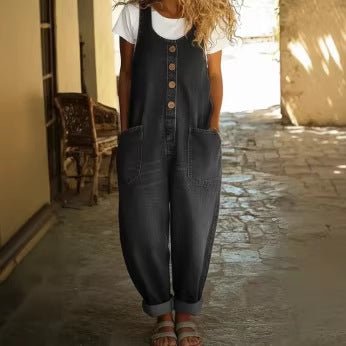 Zwarte jumpsuit in denimlook over een wit T-shirt, handen in de zakken