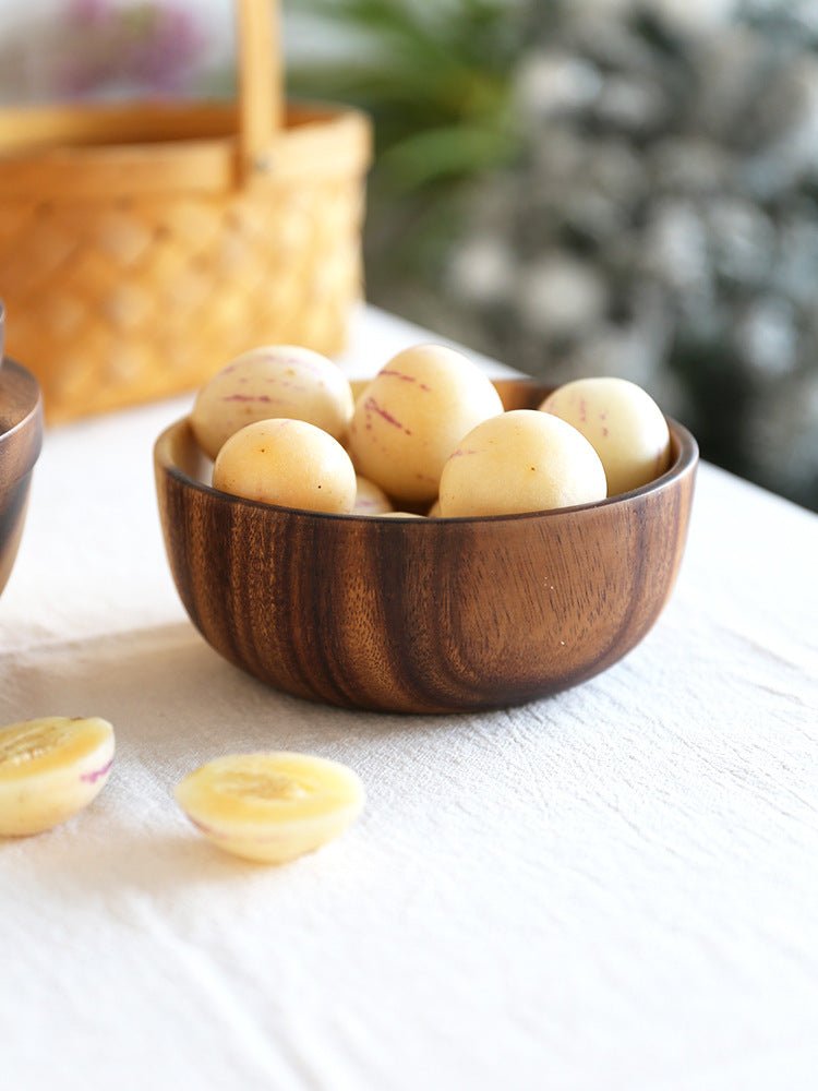 Wooden bowl with dark grain filled with small round fruits on a white table