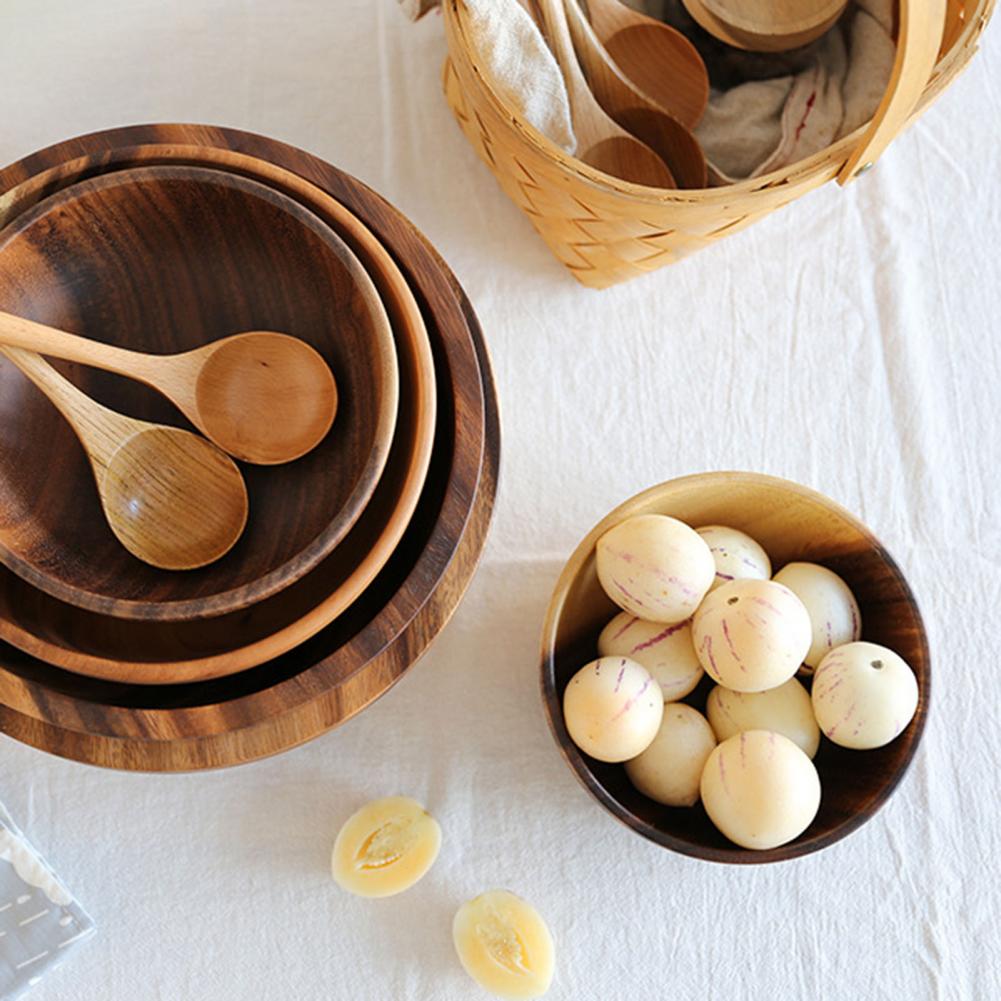 Stacked wooden bowls with dark grain, one filled with small round fruits, flat lay