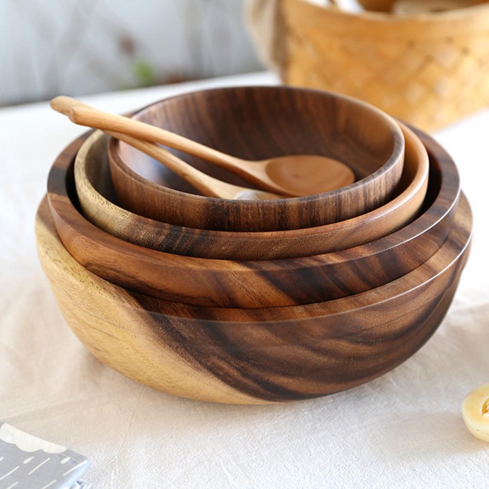 Stacked wooden bowls with dark grain, one with a wooden spoon, on a white surface
