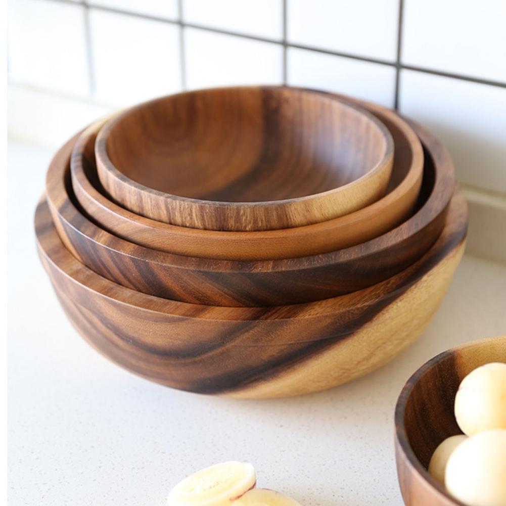 Stacked wooden bowls with dark grain on a kitchen countertop near tiled wall