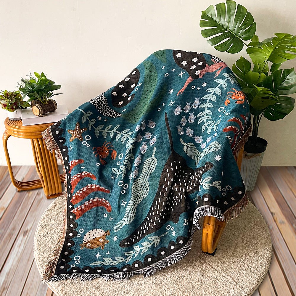 Teal woven throw with an ocean design and fringe, draped over a rattan chair